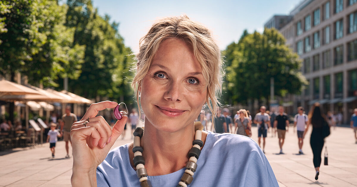 A woman holding an Oticon Reveal miniRITE hearing aid, showing how small it is