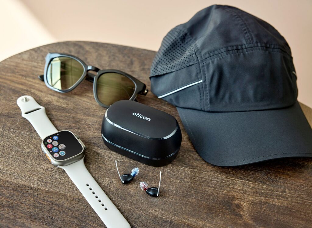 Oticon Zeal hearing aids with charging case in daily life, beside a watch and glasses